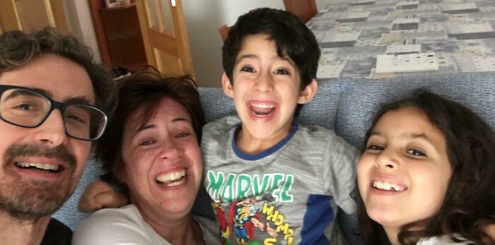 A joyful adopted family, including two parents and two kids, smiles broadly in a close-up selfie, sharing their adoption story.
