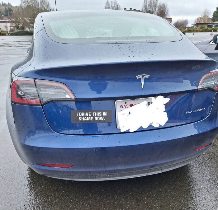 Bumper sticker on Tesla reading I drive this in shame now