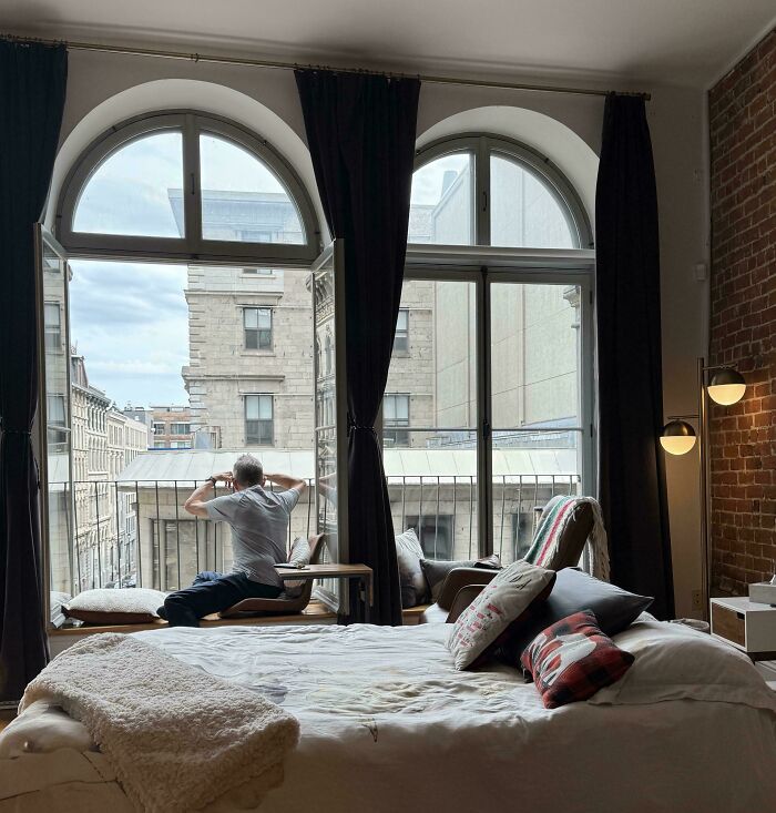 A father sits on a window sill overlooking a city street, reflecting, an amazing parent in a peaceful moment.