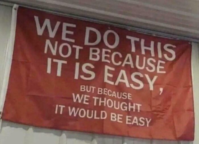 Motivational sign that reads We do this not because it is easy, but because we thought it would be easy, for entertainment at work.