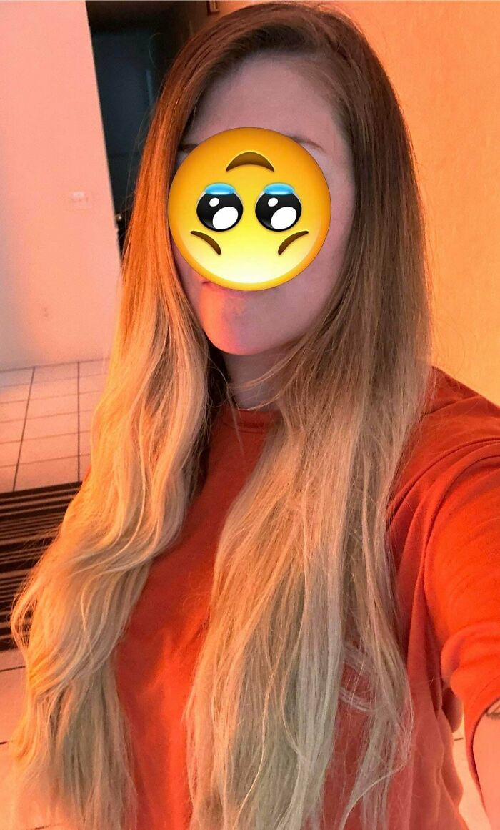 A woman showing a hair salon disaster with uneven blonde ombre hair, covering her face with a sad emoji.