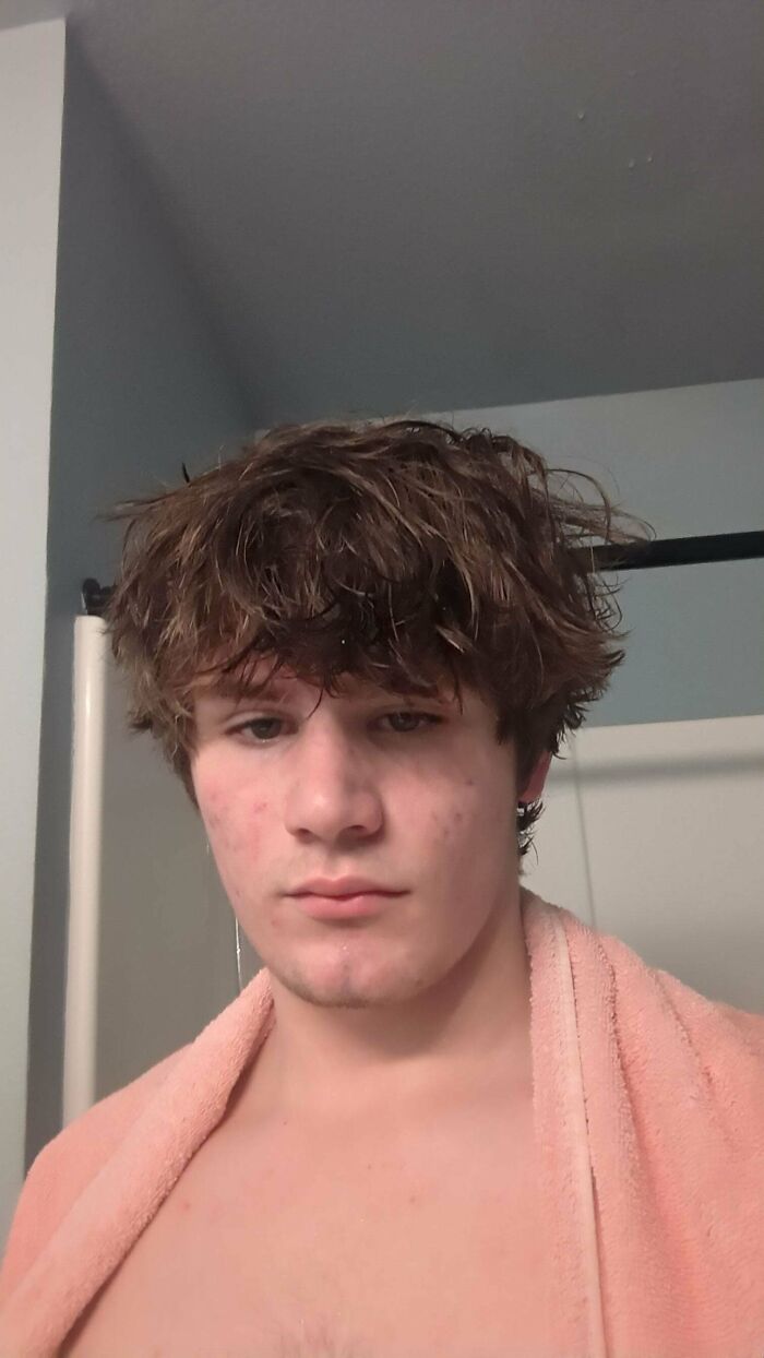 A young man with a hair salon disaster, sporting wet, messy hair that appears to be badly cut and styled, with a towel around his neck.