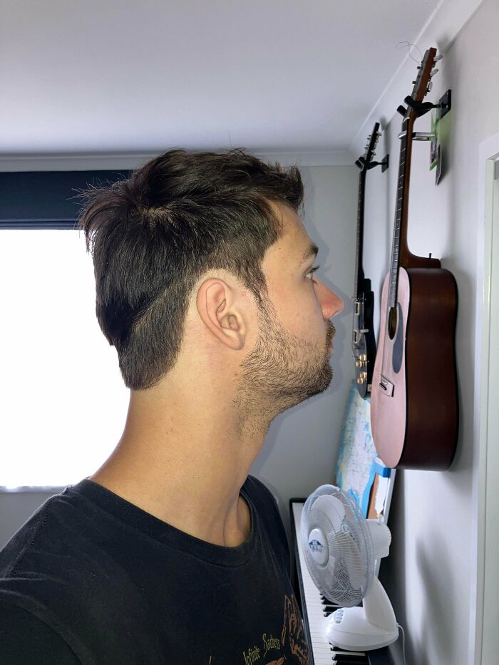 A man looking in the mirror, showing a hair salon disaster with an uneven haircut and a noticeable line shaved into his head.