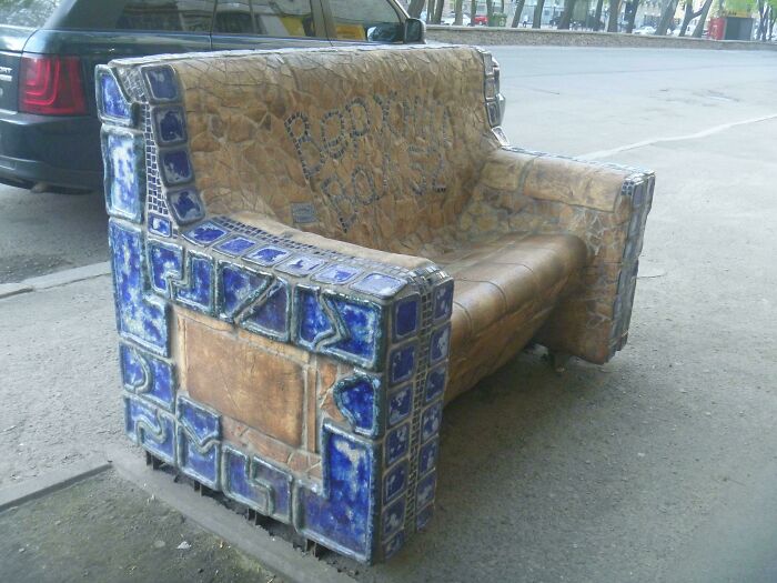 A mosaic couch, adorned with blue tiles and earthy tones, sits on a sidewalk. An interior designer could draw inspiration from this.