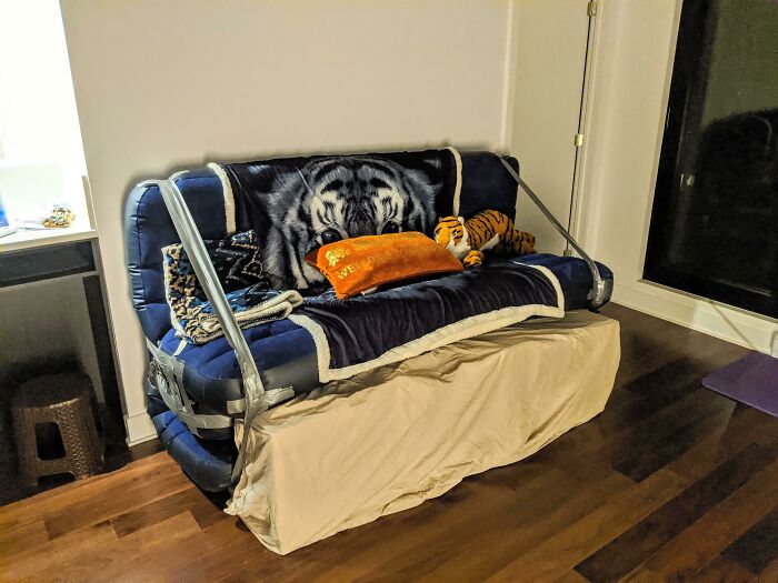 An unconventional couch, secured with tape, featuring a tiger-print blanket and plush toys. A unique piece for an interior designer.