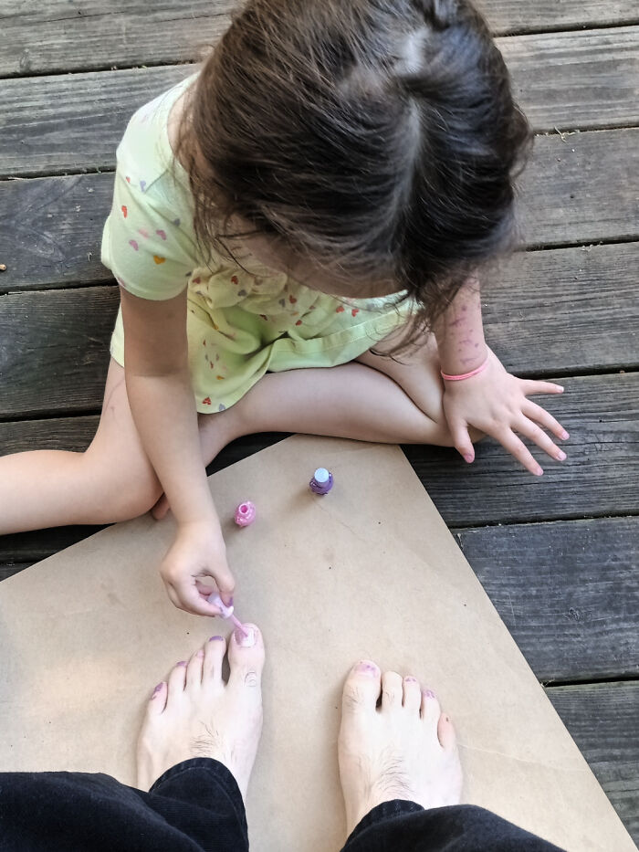 A young child painting the toenails of their father, showcasing a moment between amazing fathers and their children.