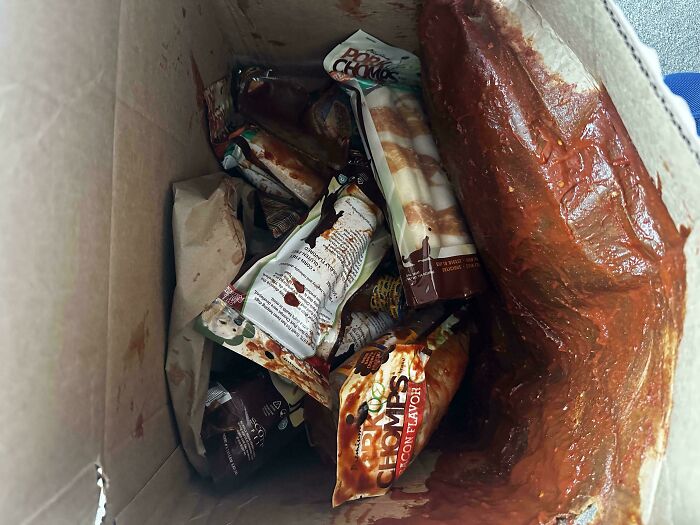 A box full of messy food delivery fails, with items spilled and sauces smeared, making cooking at home look appealing.