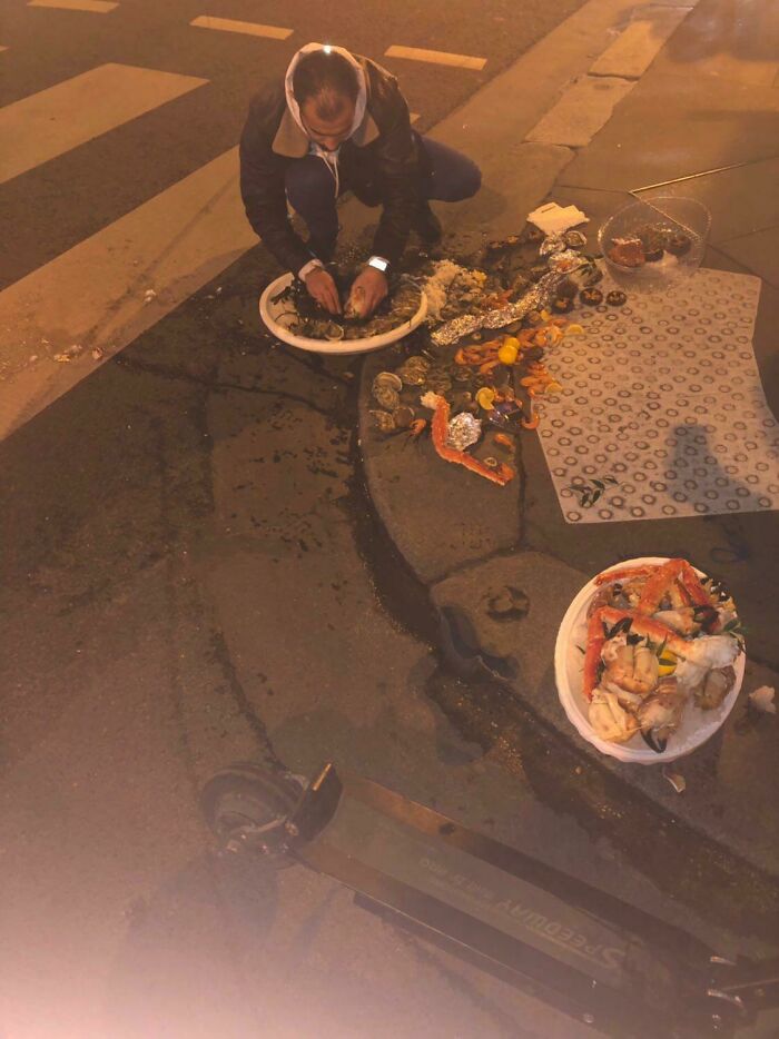 A person kneels on a sidewalk, attempting to salvage scattered seafood from a food delivery fail.