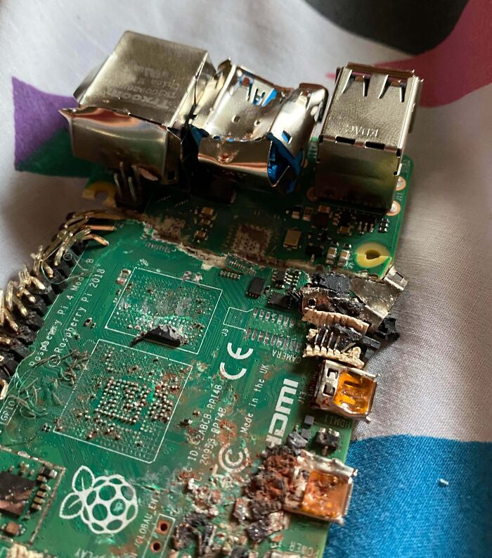 A close-up of a burnt and damaged circuit board, likely a Raspberry Pi, showing extensive Electronics Fails.