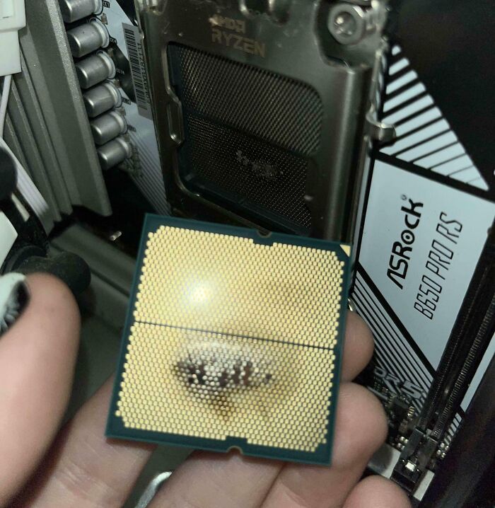 A hand holding a computer CPU with bent pins next to an empty CPU socket, demonstrating electronics fails.