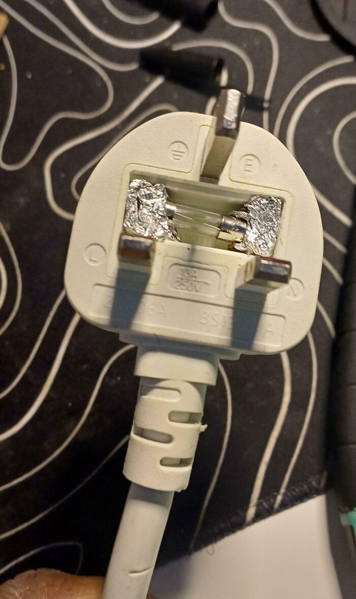A close-up of a power plug with a fuse replaced by aluminum foil, highlighting a dangerous electronics fail.