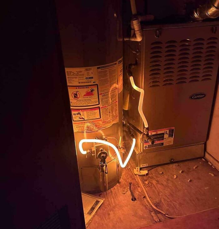 A water heater and furnace with a glowing, bent neon light, a strange example of electronics fails.