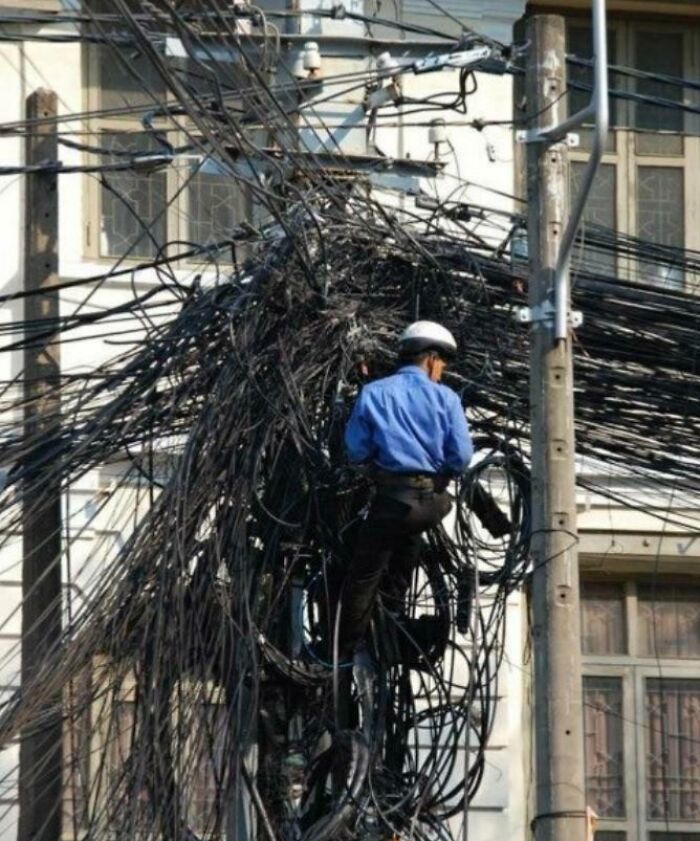 A lineman fixing a pole with numerous electronics fails, highlighting IT issues.