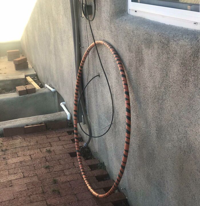 An orange and black striped hula hoop-like cable structure leaning against a concrete wall, revealing electronics fails.