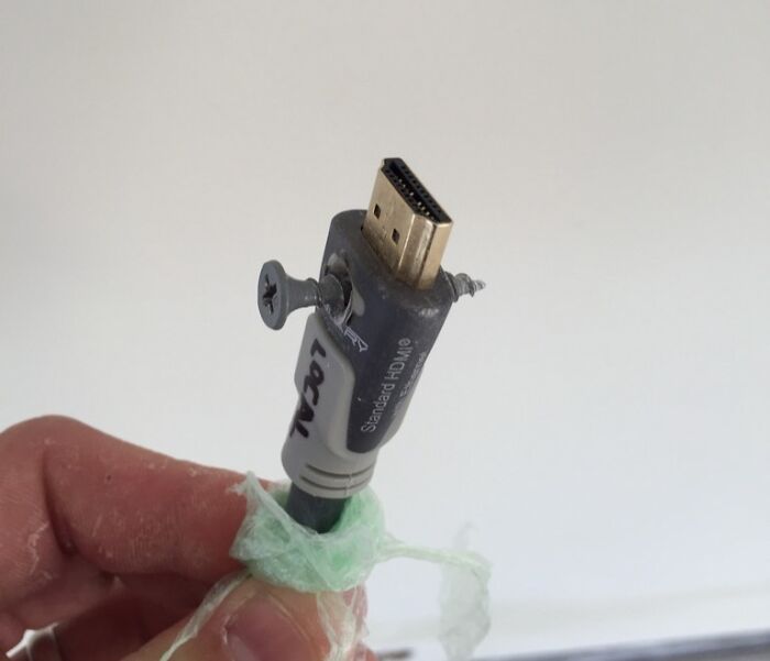 A hand holding an HDMI cable with two screws drilled through it, showcasing electronics fails.