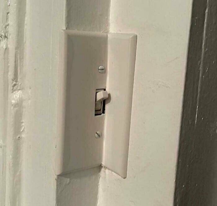 A light switch plate awkwardly installed over a door frame corner, an example of poor electronics installation.