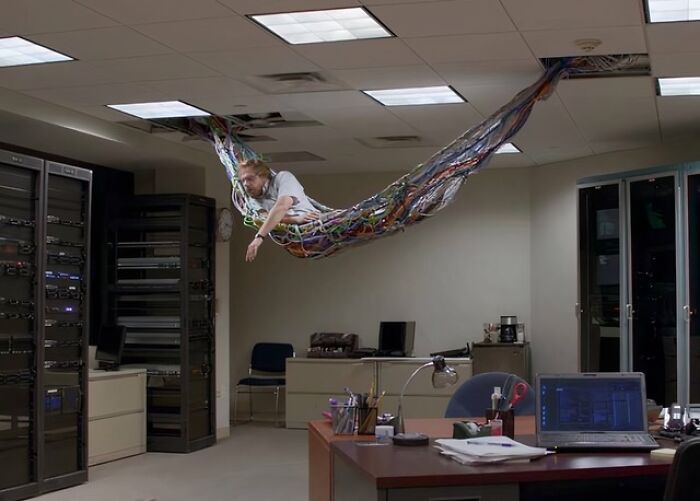 A man relaxing in a hammock made of tangled network cables hanging from a server room ceiling, an example of electronics fails and IT stress.