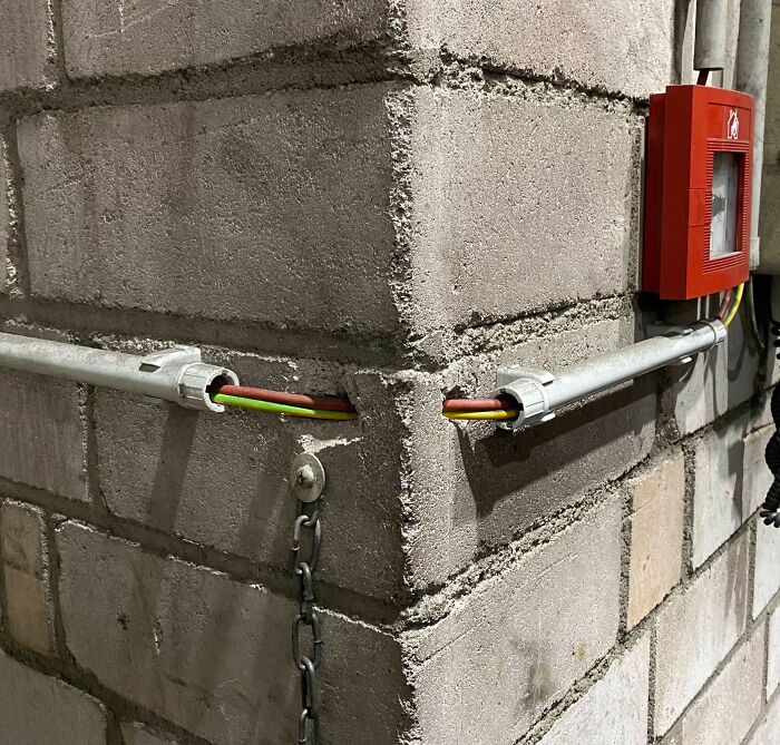 A close-up of an electronics fail where electrical wires are exposed due to poorly installed conduits on a brick wall, an IT problem.