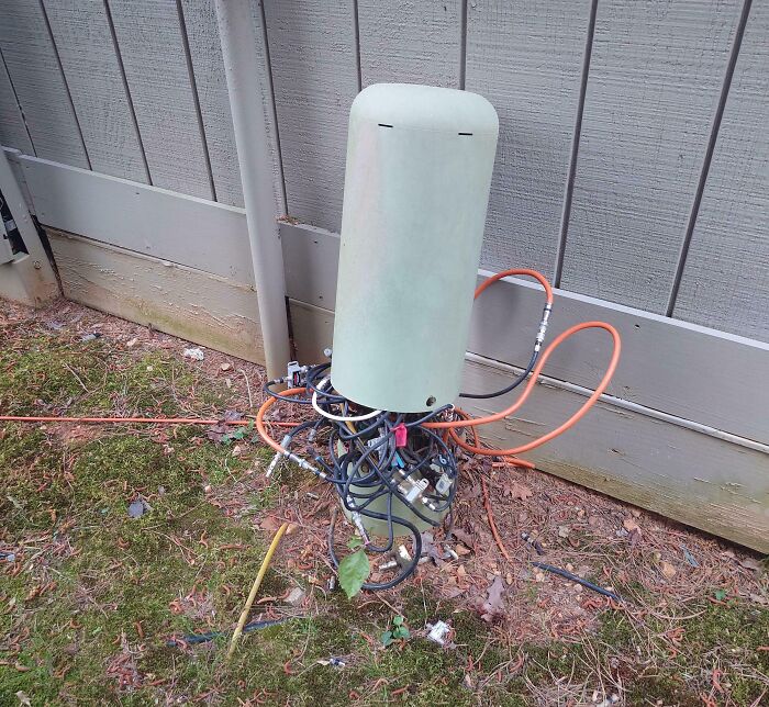 An outdoor electronics fail with a messy bundle of wires and cables spilling out from the base of a utility box, highlighting an IT issue.