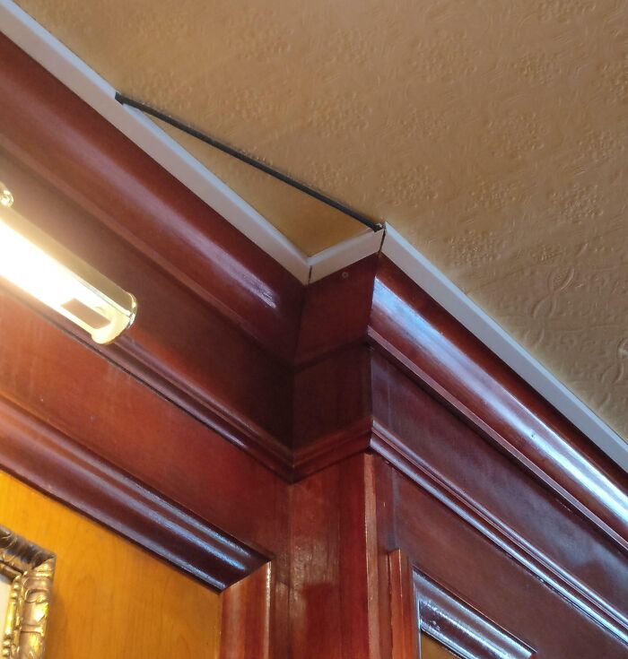 A poorly installed electrical wire running along the ceiling and wooden trim, showing electronics fails.