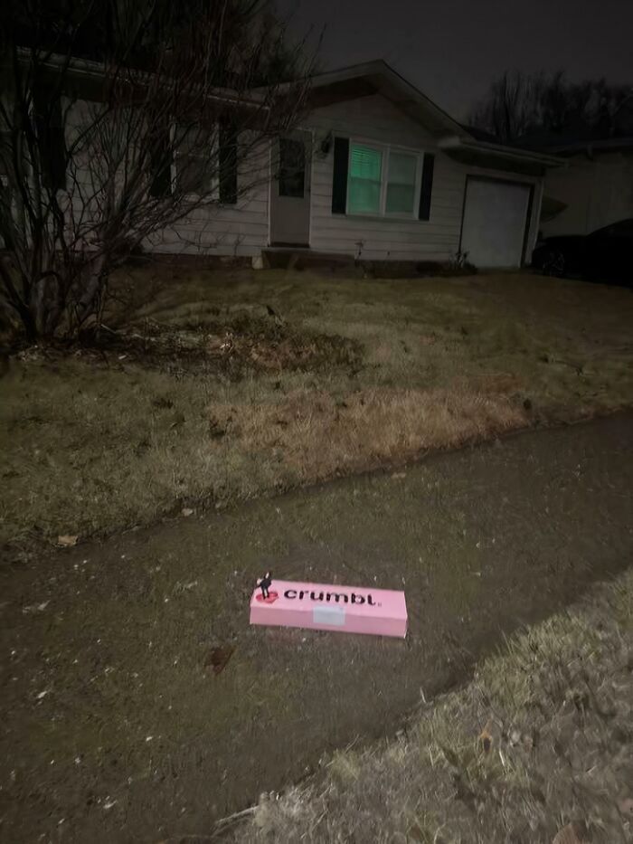 A Crumbl Cookies food delivery box left on a sidewalk, a funny food delivery fail at night.