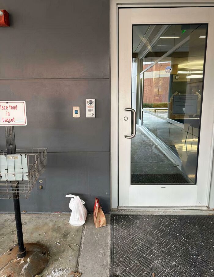 Two small paper bags are left on the ground next to a white door, despite a sign above saying place food in basket, a food delivery fail.