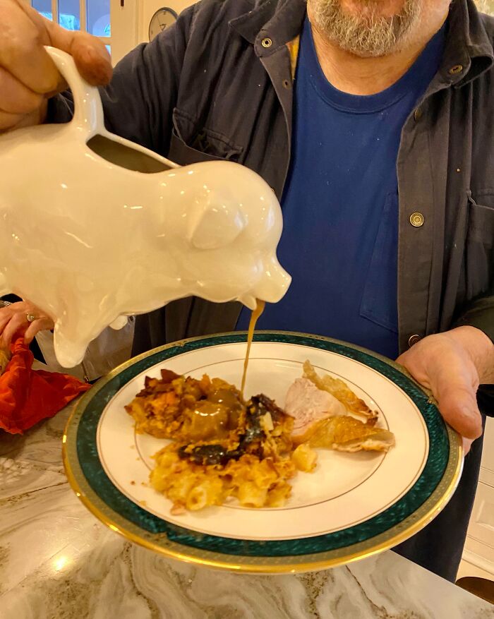 An amazing father using a pig-shaped gravy boat to pour gravy onto a plate of food, showing caring parents.