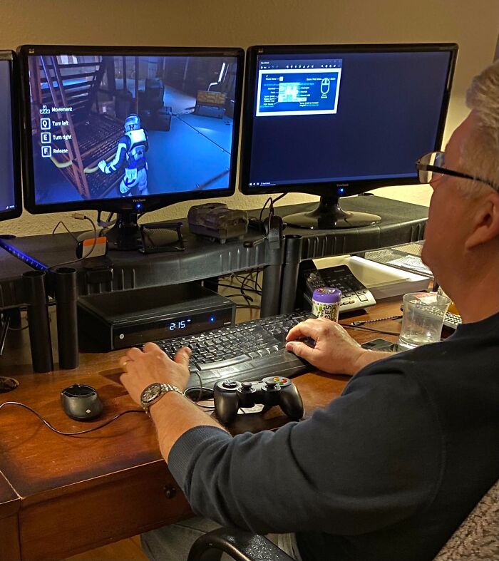 An amazing father gaming at a desk with two monitors, a keyboard, and a controller, focused on his game.