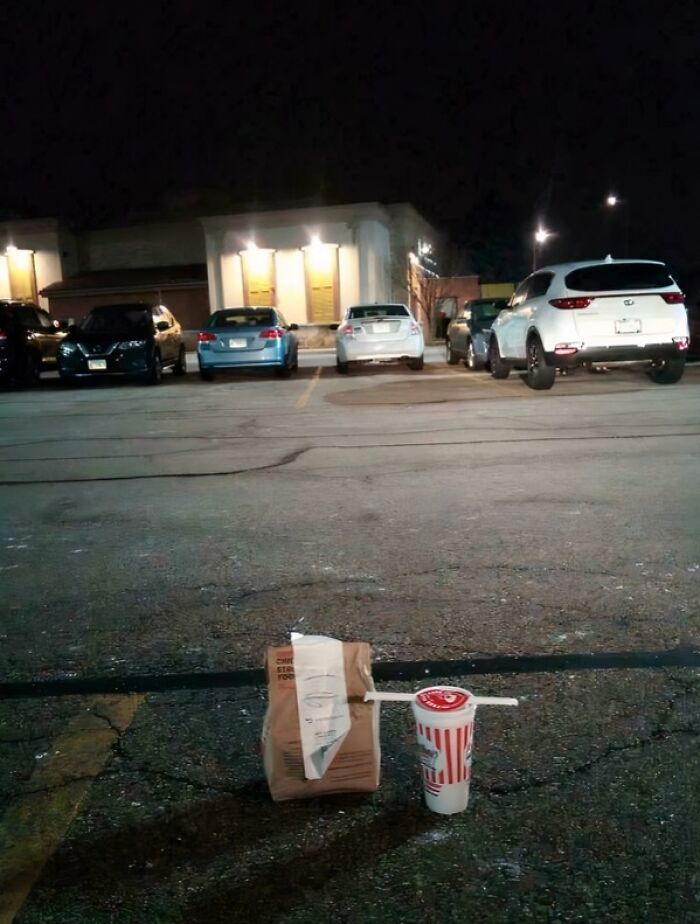 A single food delivery bag and drink left abandoned in a parking lot, a funny delivery fail.