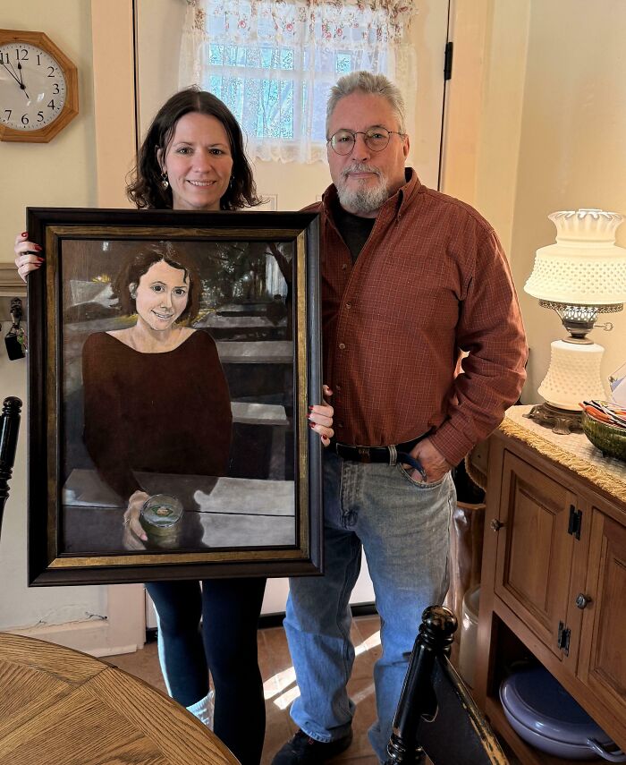 A father and daughter proudly hold a framed portrait of the daughter, demonstrating the bond of amazing parents.