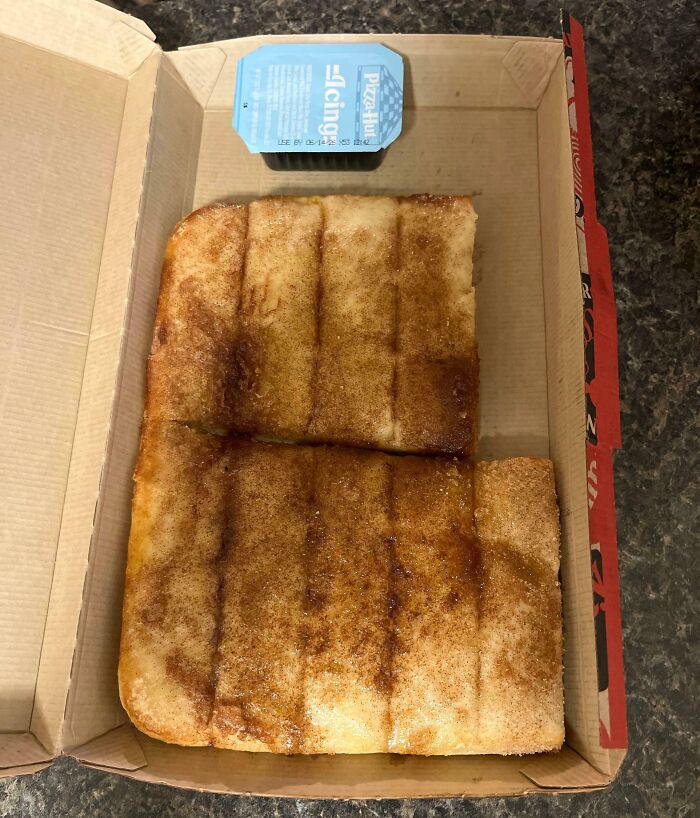A partially eaten cinnamon bread in a pizza box with icing on the side, a clear food delivery fail.