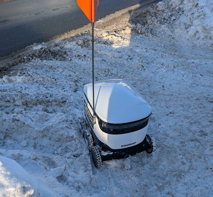 A Starship robot stuck in the snow, representing a funny food delivery fail.
