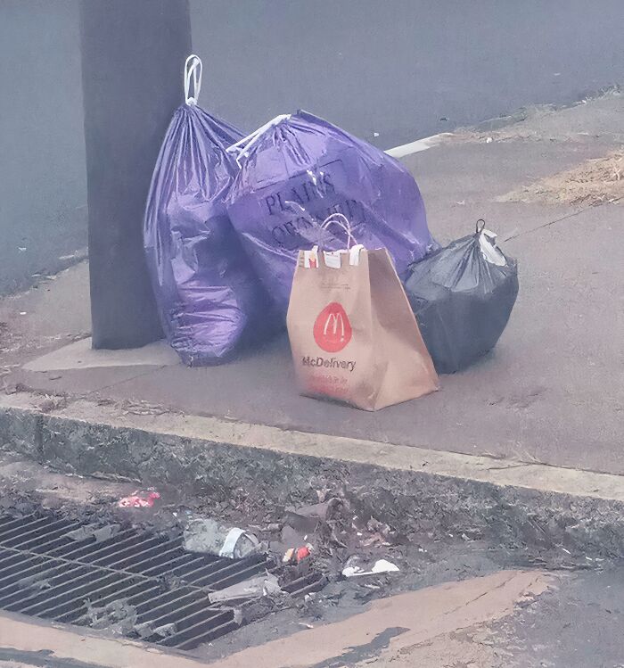 A McDonald's food delivery bag left on the ground next to three trash bags, depicting a food delivery fail.
