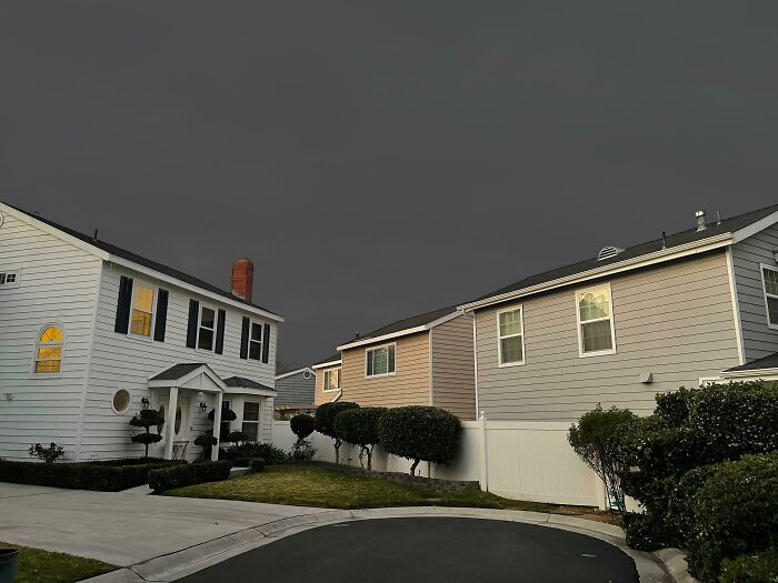 Suburban houses under a deeply unsettling dark, overcast sky, creating a liminal space.