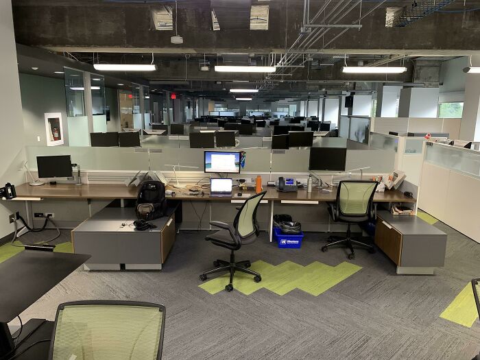 A deeply unsettling liminal space of an empty, modern office with rows of cubicles and computers, an abyss of a workplace.