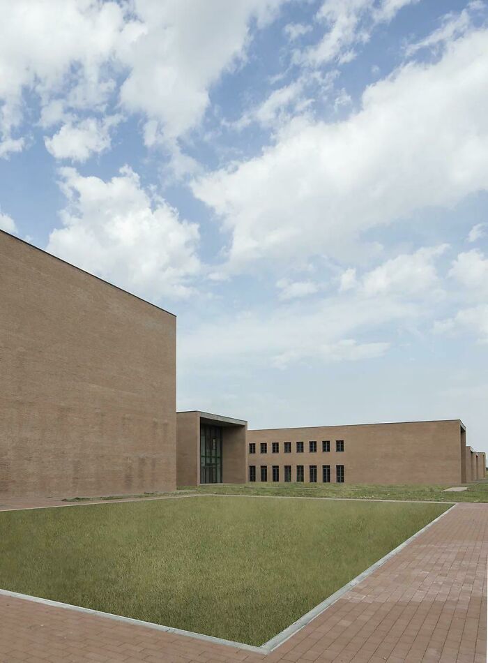 An unsettling liminal space showcasing a deserted modern brick building with sparse windows and a vast, empty lawn, an abyss of architecture.