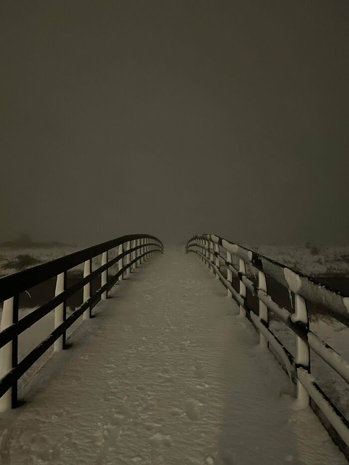 A deeply unsettling liminal space with a snow-covered bridge disappearing into thick fog, creating an eerie, endless abyss.