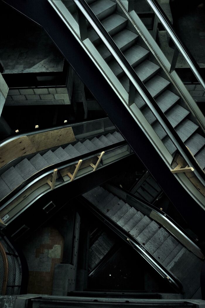 Multiple escalators crisscrossing in a dark, abandoned station, creating an unsettling liminal space.