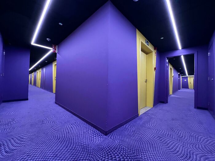 Vibrantly purple and yellow hotel hallway, creating a disorienting and unsettling liminal space.