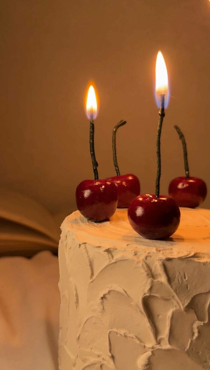 A handmade cake with cherry-shaped candles, showcasing talent and a little magic in its unique design.