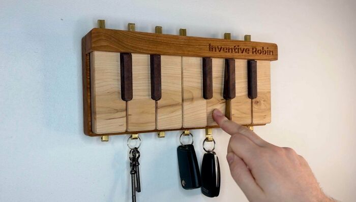 A finger pressing a key on a handmade wooden piano-themed key holder on a white wall, displaying talent.