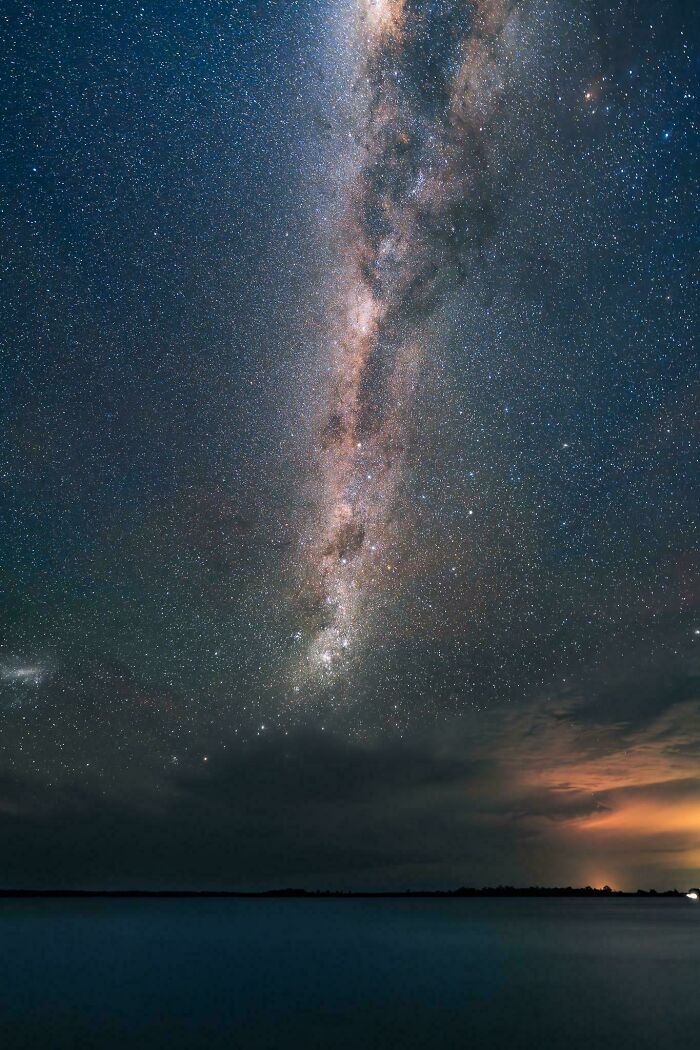 The breathtaking Milky Way galaxy stretches across a dark sky above a body of water, an interesting post for an Aussie.