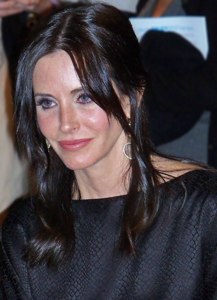 Close-up portrait of Courteney C*x with dark hair and blue eyes at an event