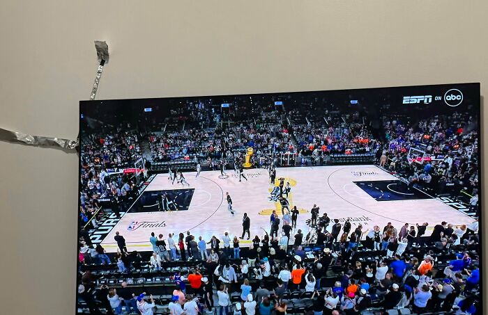A large TV displaying a basketball game with a makeshift antenna made of aluminum foil, a clever solution.