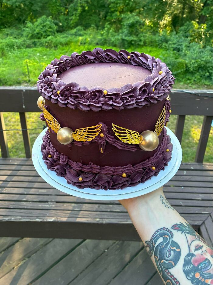 A purple cake with golden snitch decorations, a magical and delicious treat created by bakers.