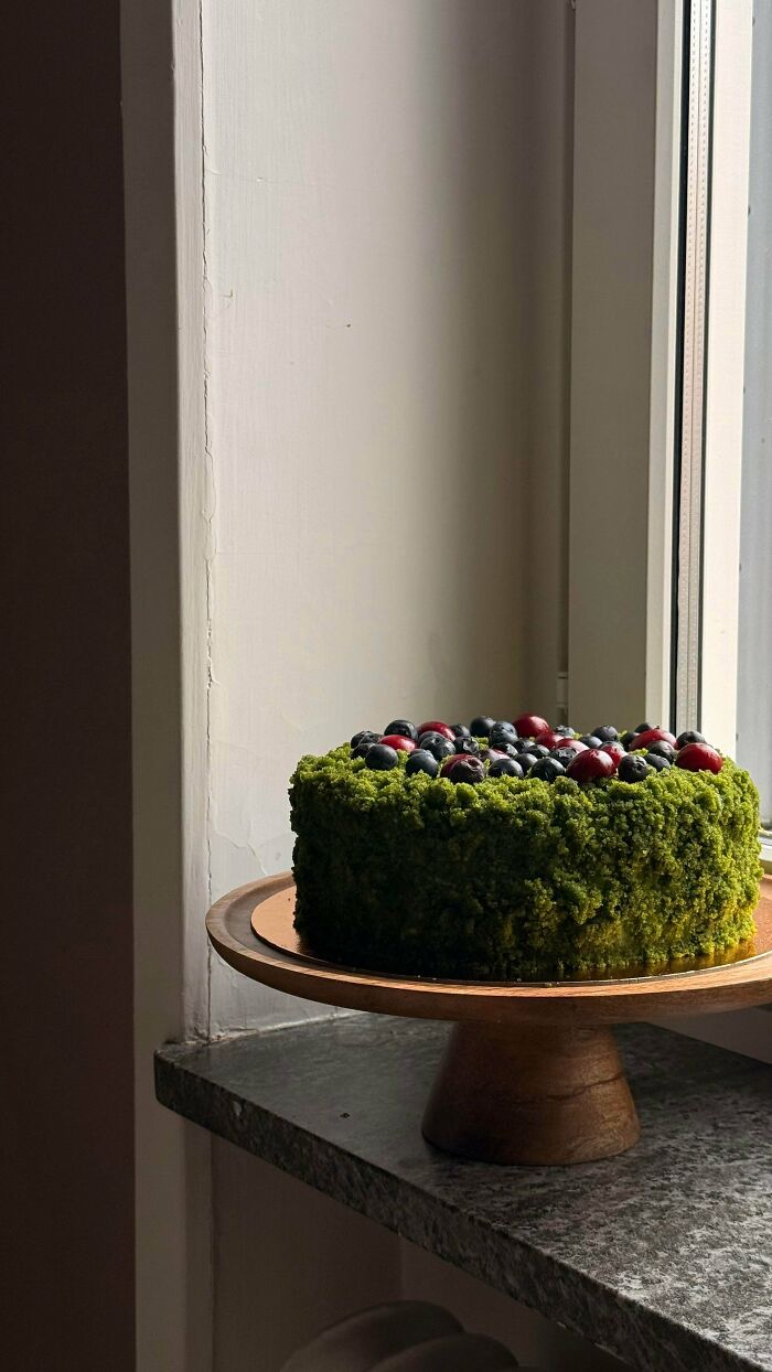 A green cake topped with blueberries and cranberries, a beautiful and delicious treat by bakers.