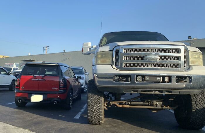 Huge lifted Ford truck parked next to regular car in American parking lot