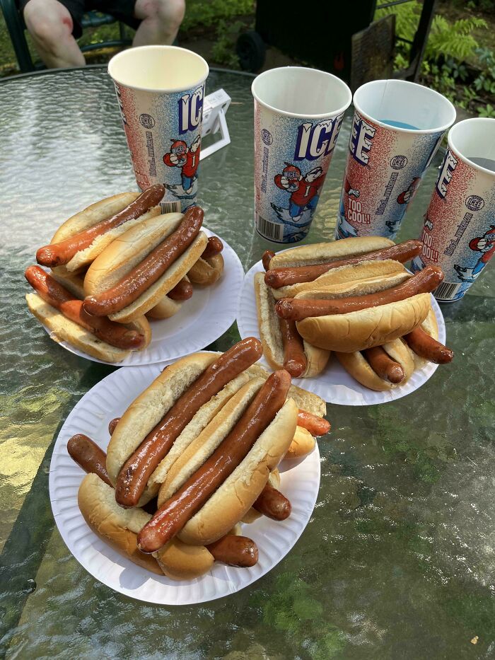 Multiple hot dogs and large American ice drinks on outdoor glass table