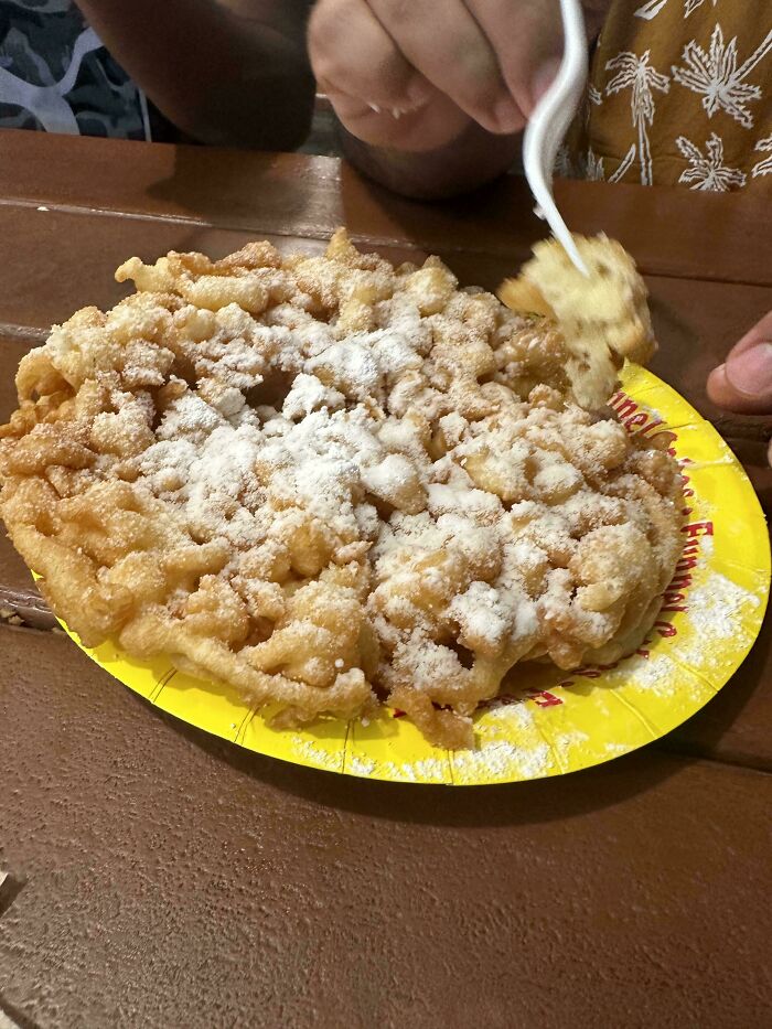 Person eating funnel cake dusted with powdered sugar on a yellow plate