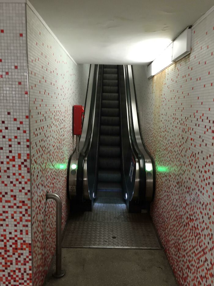 Deeply unsettling liminal space featuring a narrow escalator descending between red and white tiled walls.